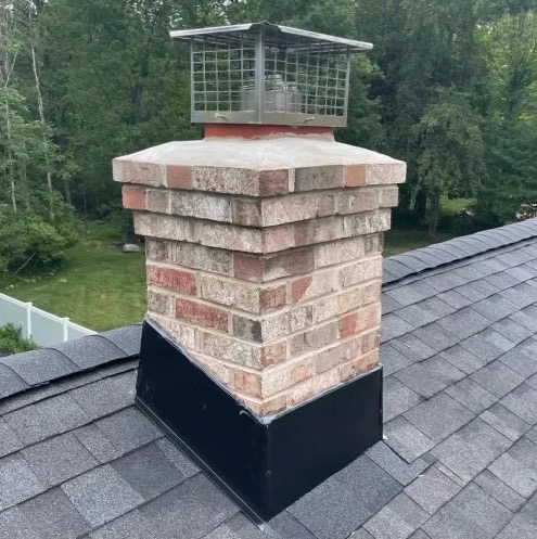 A brick chimney with a stainless steel spark arrestor cap and black flashing base