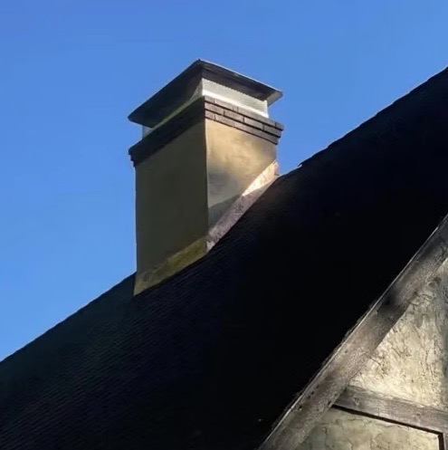 Stucco chimney topped with a brick and concrete crown above a dark shingled roof