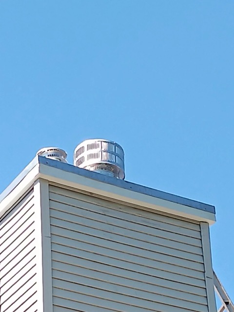 New metal chimney caps installed on a tan sided structure against a blue sky