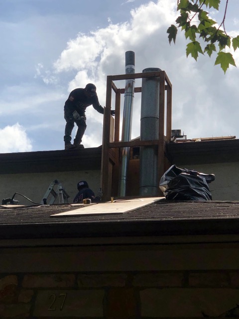 A Top Notch 1 technician installing metal chimney flue pipe inside a wooden chimney frame on a rooftop