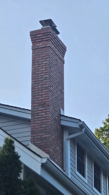 Tall brick chimney with a metal cap rising above a light gray sided house with white trim