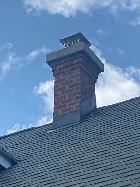 Red brick chimney with a metal cap and flashing on a slate roof in New Jersey