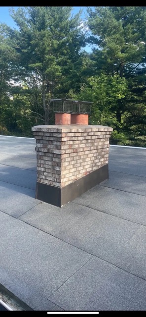 Brick chimney with exposed clay flue liners and metal flashing on a flat rubber membrane roof